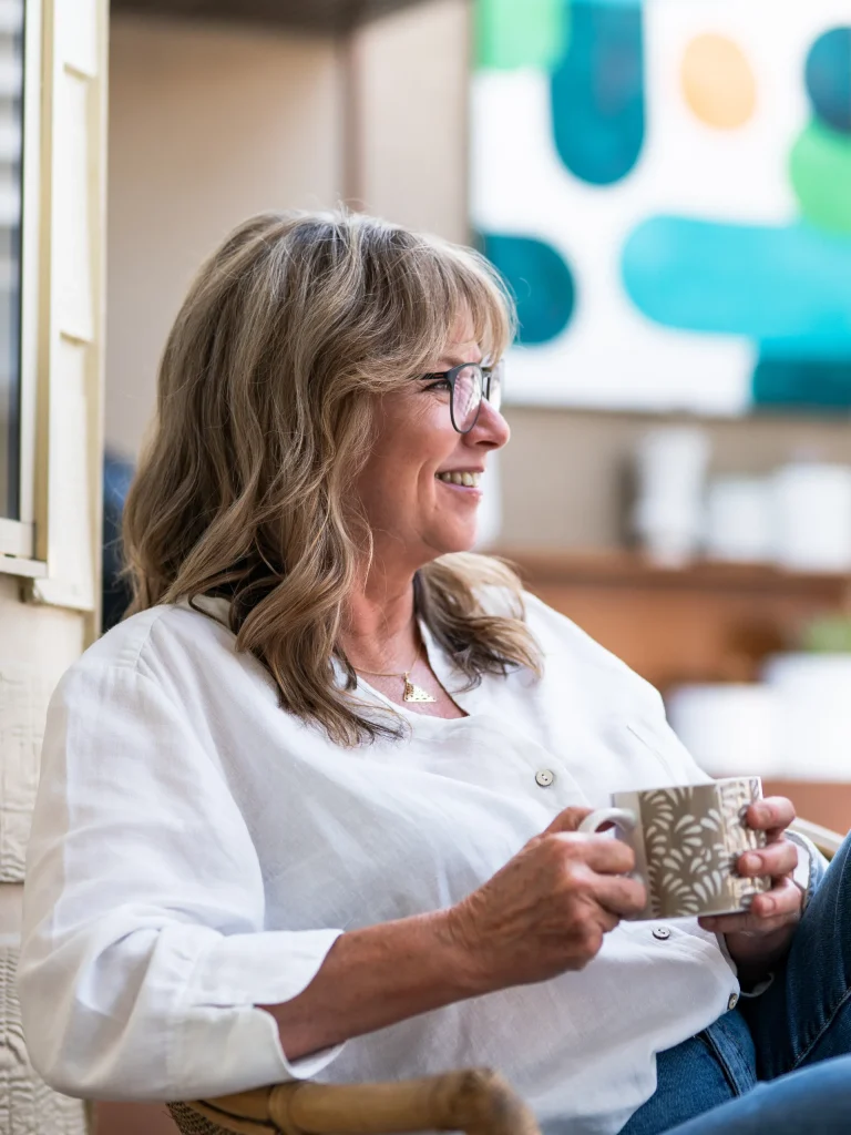 Kimberly sitting side on in a chair outside, a coffee cup in her hand