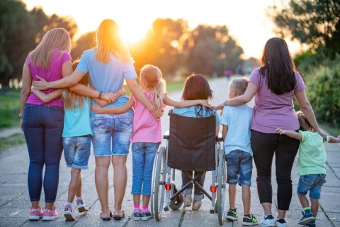 A group of people, young and older, one in a wheelchair, with linked arms watching the sunrise.