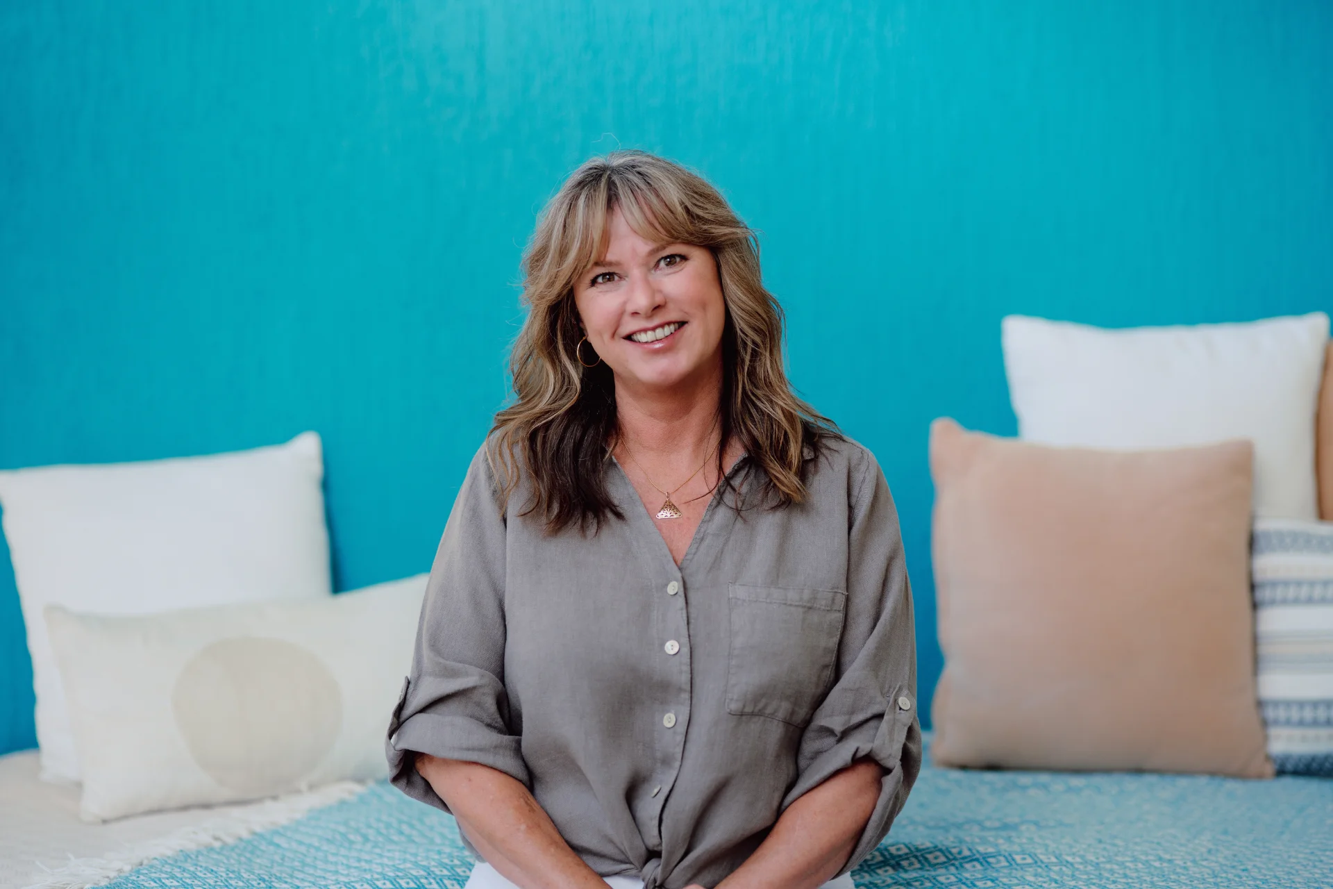 Kimberley sitting, facing forward, a turquoise wall and pillows in the background.