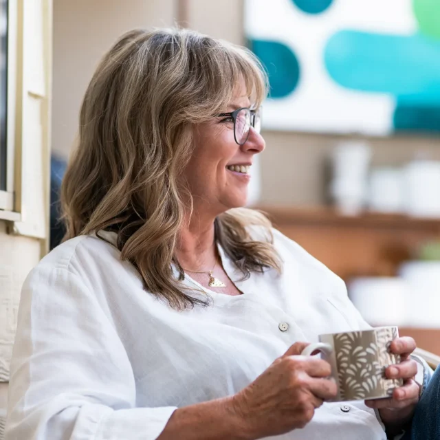 Kimberly sitting side on in a chair outside, a coffee cup in her hand